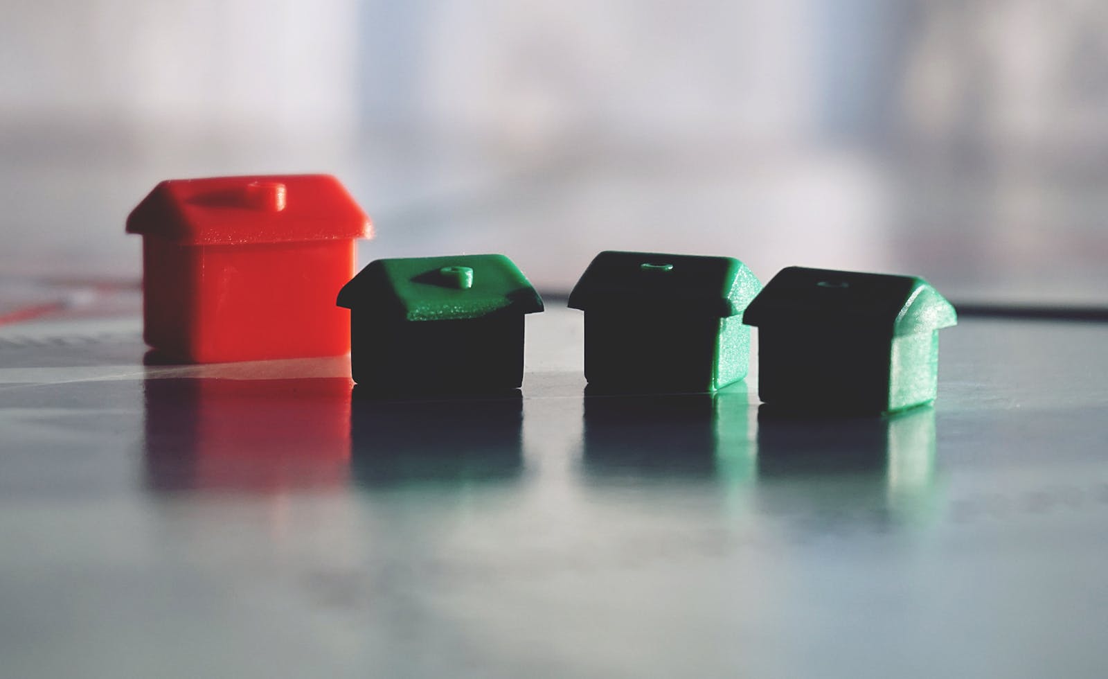 Close-up photo of red and green Monopoly game houses on a reflective surface. Fortify Loans - Tasmania based Mortgage brokers for Investment Property Loans